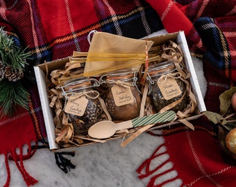 May include: A gift box filled with three glass jars of loose leaf tea blends. The jars are labeled "Merry Gatherings", "Garden Holiday", and "Winter Gatherings". The box also includes a wooden spoon and a bag of honey sticks.