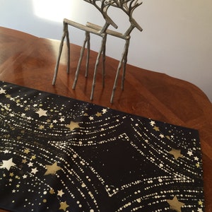 May include: A black table runner with a gold star and dot pattern. Two silver reindeer figurines are on the table.