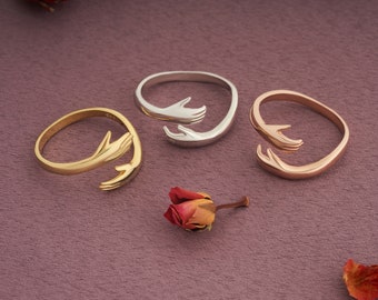May include: Three rings with a design of two hands holding each other. The rings are in gold, silver, and rose gold.