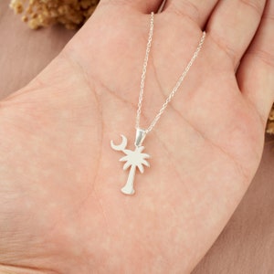 Op de afbeelding: Een zilveren ketting met een palmboom en halve maan hanger. De ketting ligt op een hand.