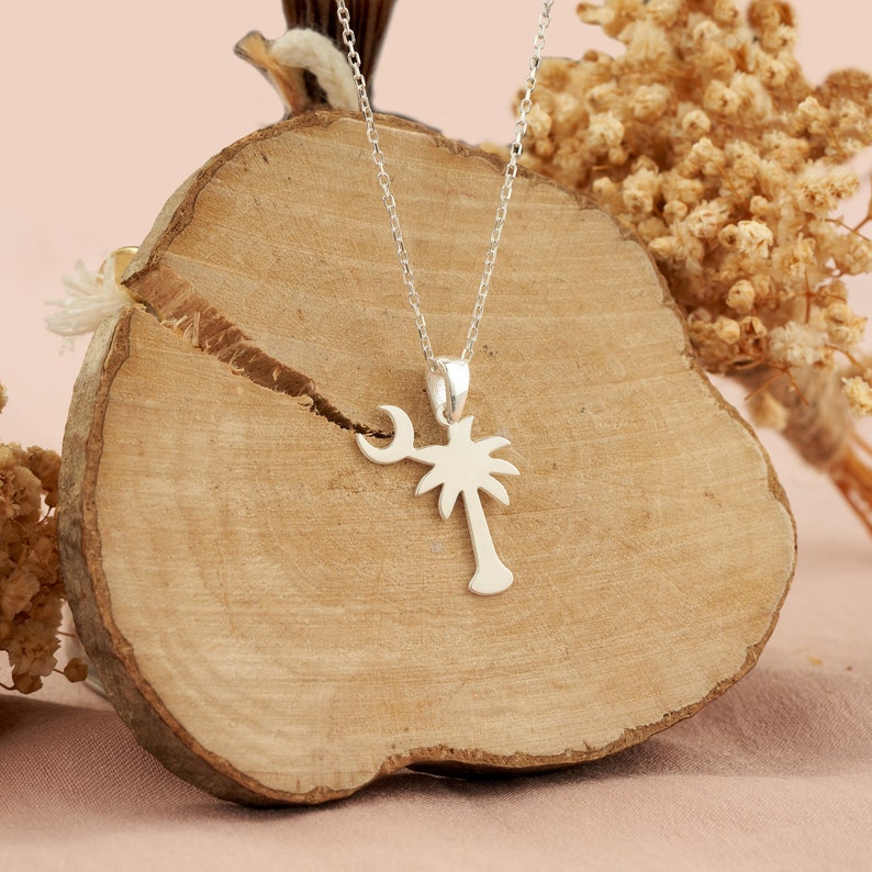Op de afbeelding: Zilveren ketting met een palmboom hanger. De palmboom is gesilhouetteerd en heeft aan de ene kant een halve maan.