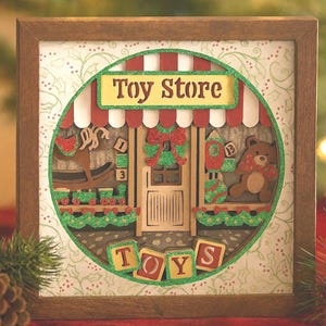 May include: A framed, layered wooden art piece depicting a toy store. The store has a red and white striped awning, a door, and various toy displays, including a rocking horse and a teddy bear. The word "TOYS" is spelled out at the bottom.
