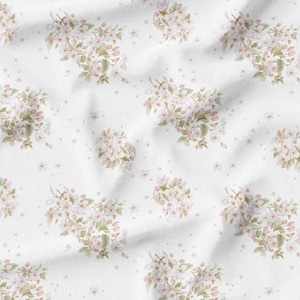 May include: White fabric with a repeating pattern of watercolor-style floral clusters. The flowers are a soft pink with green leaves, and small pink dots are scattered across the background. The fabric has a slightly wrinkled texture.