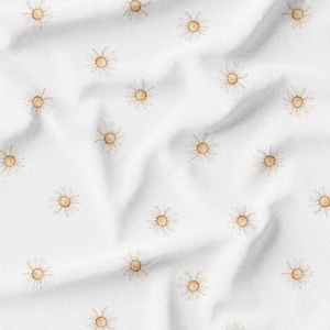 May include: White fabric with a repeating pattern of watercolor suns. Each sun has a yellow center and thin, radiating lines. The fabric is creased, creating shadows and texture.