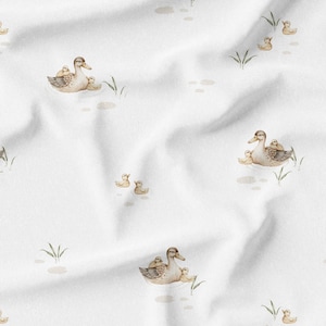 May include: White fabric with a repeating pattern of watercolor ducks and ducklings. The ducks are in shades of brown and tan, with some ducklings riding on their backs. Green grass and water details are also present.