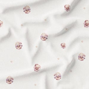 May include: White fabric with a repeating pattern of watercolor-style flowers in shades of pink and purple, interspersed with small, light-brown dots. The fabric has a soft, textured appearance with gentle folds.
