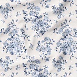 May include: A white fabric with a repeating pattern of blue floral bouquets and foliage. The design features large, stylized flowers and smaller sprigs, creating a classic, elegant aesthetic. The fabric has a slightly wrinkled texture.