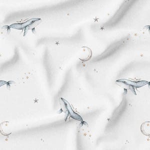 Może przedstawiać: Biała tkanina z powtarzającym się wzorem wielorybów, księżyców i gwiazd w akwareli. Wieloryby są jasnoniebieskie z małymi łódkami na grzbietach. Księżyce są w kształcie półksiężyca z wiszącymi gwiazdami, a gwiazdy są małe i rozproszone.