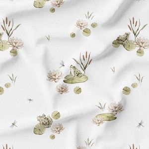 May include: White fabric with a repeating pattern of watercolor illustrations. The design features frogs on lily pads, lotus flowers, cattails, dragonflies, and lily pads in shades of green, beige, and brown.