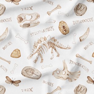 Op de afbeelding: Een witte achtergrond met een herhalend patroon van dinosaurusbotten, fossielen en de namen van verschillende dinosaurussen, waaronder T-Rex, Stegosaurus, Triceratops en Diplodocus.