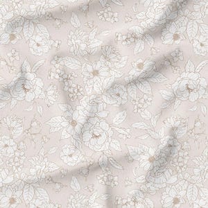 May include: A fabric with a repeating floral pattern. The design features white and light brown flowers and leaves on a light pink background. The fabric has visible folds and creases, adding texture to the design.