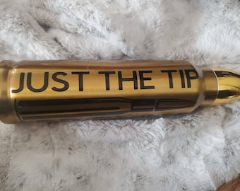 May include: A gold-colored bullet-shaped object with the words "JUST THE TIP" in black lettering. The object has a shiny, metallic finish and a detailed design, resembling a large bullet. The background is a soft, textured, light gray surface.
