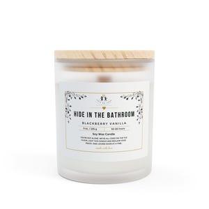 Puede incluir: Un tarro de vela de vidrio blanco esmerilado con una tapa de madera. La etiqueta dice "Hide in the Bathroom Blackberry Vanilla Soy Wax Candle 9 oz / 255 g 50-60 hours You're not alone, we've all cried on the tile floor. Light this candle and reclaim your peace - one locked door at a time. Made with love."