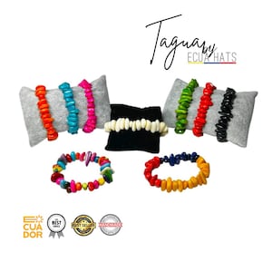 May include: Assortment of colorful wooden bracelets with different designs and colors. The bracelets are displayed on gray and black fabric surfaces. The text "Taguapy Ecua Hats" is visible in the top right corner of the image.