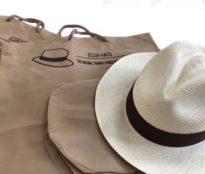 May include: Two brown canvas bags with the text "Ecua Hats The Original "Panama" is Made in Ecuador" printed on them. A white Panama hat with a brown ribbon is sitting on top of the bags.
