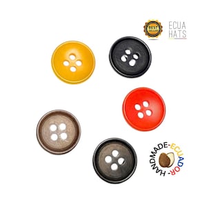 Può includere: Una collezione di cinque bottoni rotondi in vari colori: giallo, nero, rosso, marrone e grigio scuro. Ogni bottone ha quattro fori per cucire. L'immagine include il testo "ECUA HATS" e "HANDMADE-ECUADOR".