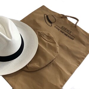 May include: A white Panama hat with a black band, packaged in a brown canvas bag with the text "Ecua Hats The Original Panama is Made in Ecuador".