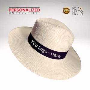 Puede incluir: Un sombrero de paja blanco con una banda negra que dice "You Logo - Here". El sombrero es de estilo cl&aacute;sico con un ala ancha y una corona ligeramente puntiaguda.