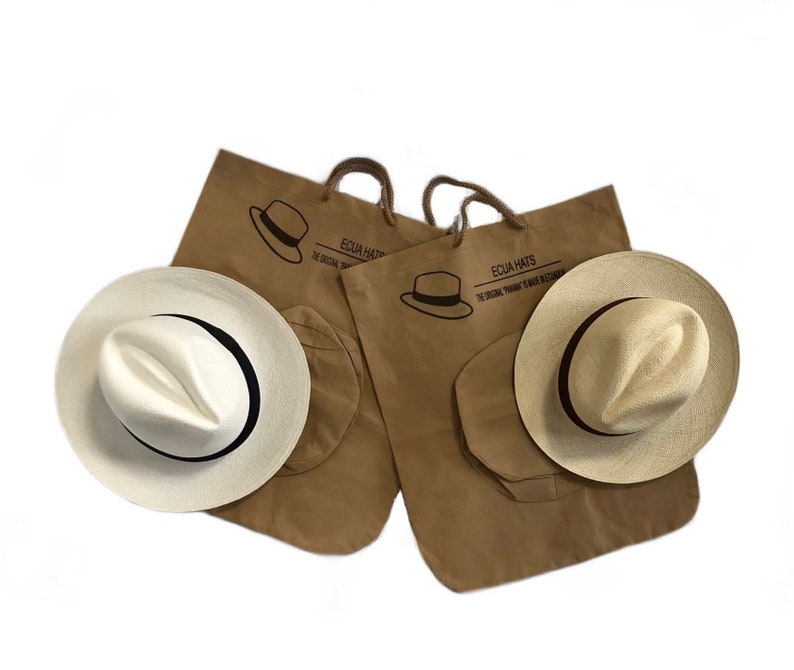 May include: Two brown paper bags with the text "Ecua Hats" and "The Original Panama  Toquilla Straw Hats" printed on them. Each bag contains a white Panama hat with a black ribbon.