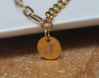 May include: A gold chain bracelet with a round charm featuring the letter "J" engraved on it.
