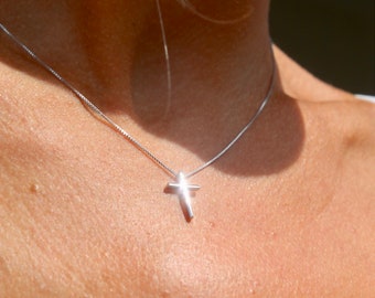 May include: A silver chain necklace with a small, simple silver cross pendant.