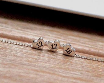 May include: Silver necklace with three heart-shaped charms. Each charm has a number engraved on it: 12, 12, and 18.