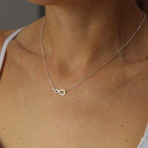 May include: A silver infinity necklace with a small clear stone accent. The necklace is worn by a model.