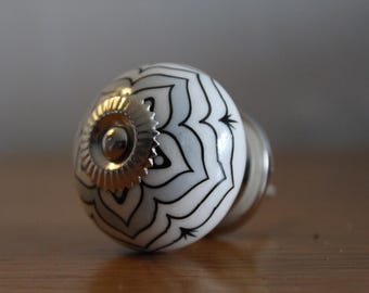 May include: A white and black patterned cabinet knob with a gold-colored metal base. The knob has a round shape with a floral design. The hardware is designed for furniture and home decor.