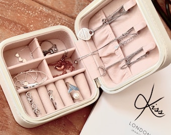 May include: A white jewelry box with compartments for rings, earrings, and necklaces. The box is open and filled with silver jewelry. The box has the text "Kiss London Jewellery" on the front.