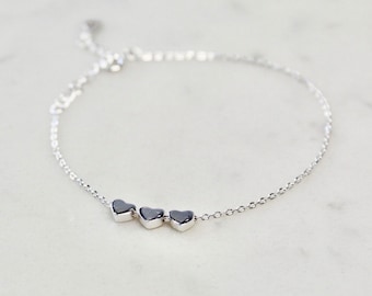 May include: A silver chain bracelet with three small heart charms.