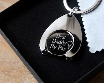 May include: Silver golf ball holder keychain with the inscription "Best Daddy By Par" and a golf club icon.