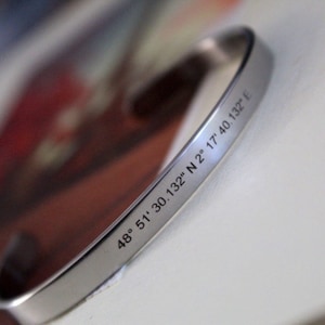 Puede incluir: Pulsera de plata con coordenadas grabadas: 48° 51' 30.132" N 2° 17' 40.132" E