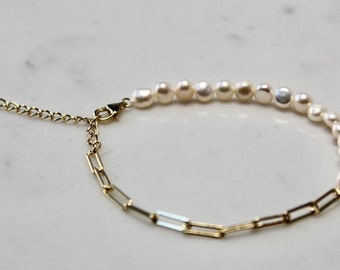 May include: A gold chain bracelet with a row of white pearls. The bracelet has a lobster clasp closure.