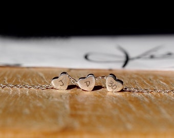 May include: A silver chain necklace with three heart-shaped charms. Each charm has a letter engraved on it: J, D, and 30.