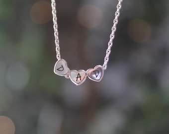 May include: Silver necklace with three heart-shaped charms, each with a letter engraved on it, spelling out "DAD".