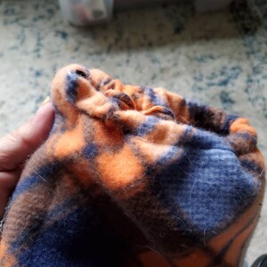 Könnte beinhalten: Eine blaue und orangefarbene karierte Fleece-Stofftasche mit Kordelzug.