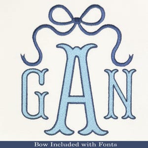 May include: Light blue embroidered monogram with the letters G, A, and N, topped with a navy blue bow. The letters have a decorative, ornate font. The text "Bow Included with Fonts" is at the bottom.