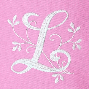 K&ouml;nnte beinhalten: Wei&szlig; gestickter Buchstabe L mit floralen Verzierungen auf einem rosa Stoffhintergrund.