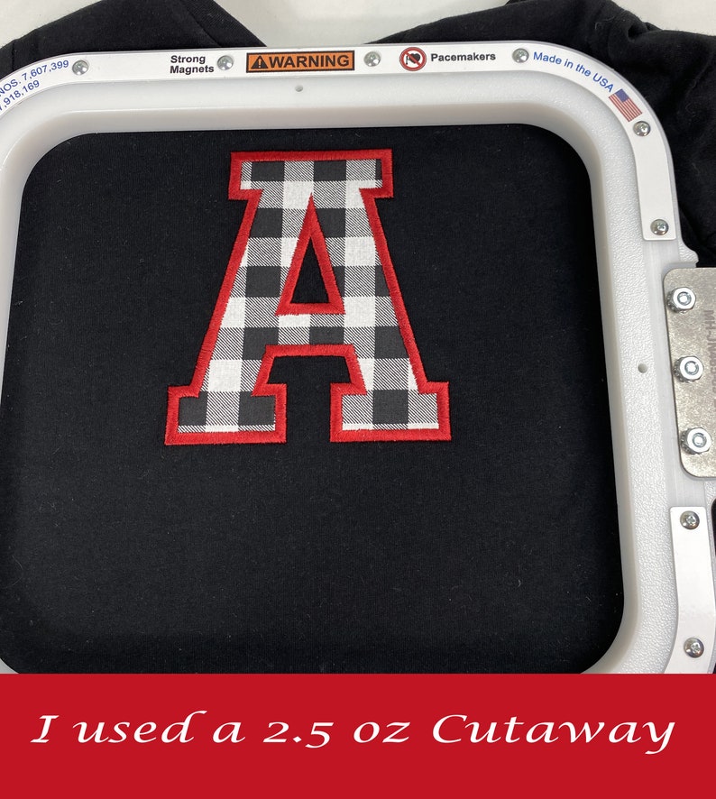 May include: A black and white checkered letter A with a red outline is being embroidered on a black fabric in a white embroidery hoop. The text "I used a 2.5 oz Cutaway" is at the bottom of the image.