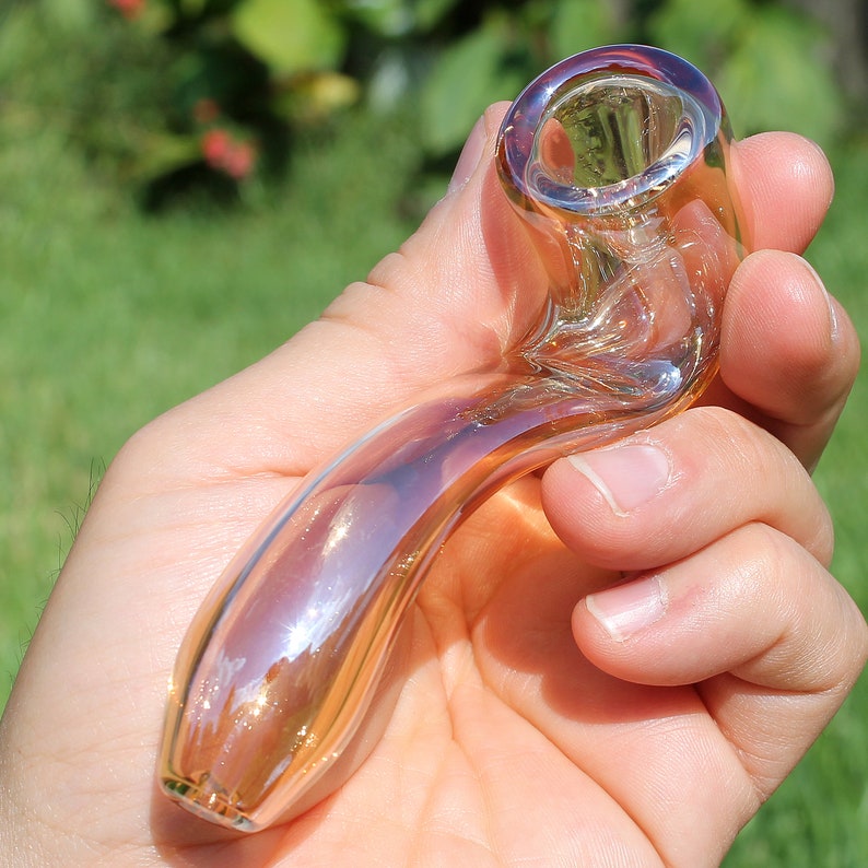 May include: A clear glass pipe with a iridescent finish. The pipe is shaped like a curved tube with a bowl at one end and a mouthpiece at the other.