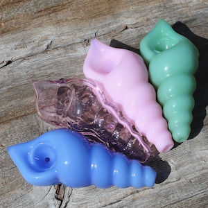 May include: Four glass seashell-shaped pipes in different colors: pink, purple, blue, and green. The pipes are all hand-blown and have a unique, organic shape.