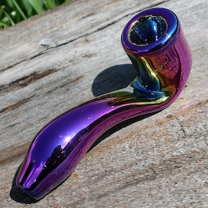 May include: A rainbow iridescent glass pipe with a curved stem and a round bowl. The pipe is made of glass and has a smooth, shiny finish.