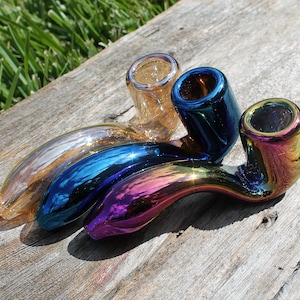 Może przedstawiać: Trzy szklane fajki z iryzującymi wykończeniami w odcieniach złota, niebieskiego i fioletowego. Fajki są ułożone w zakrzywiony kształt, z złotą fajką na górze i fioletową fajką na dole.