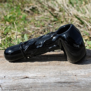 May include: A black glass smoking pipe with a wavy design. The pipe has a bowl on one end and a mouthpiece on the other.