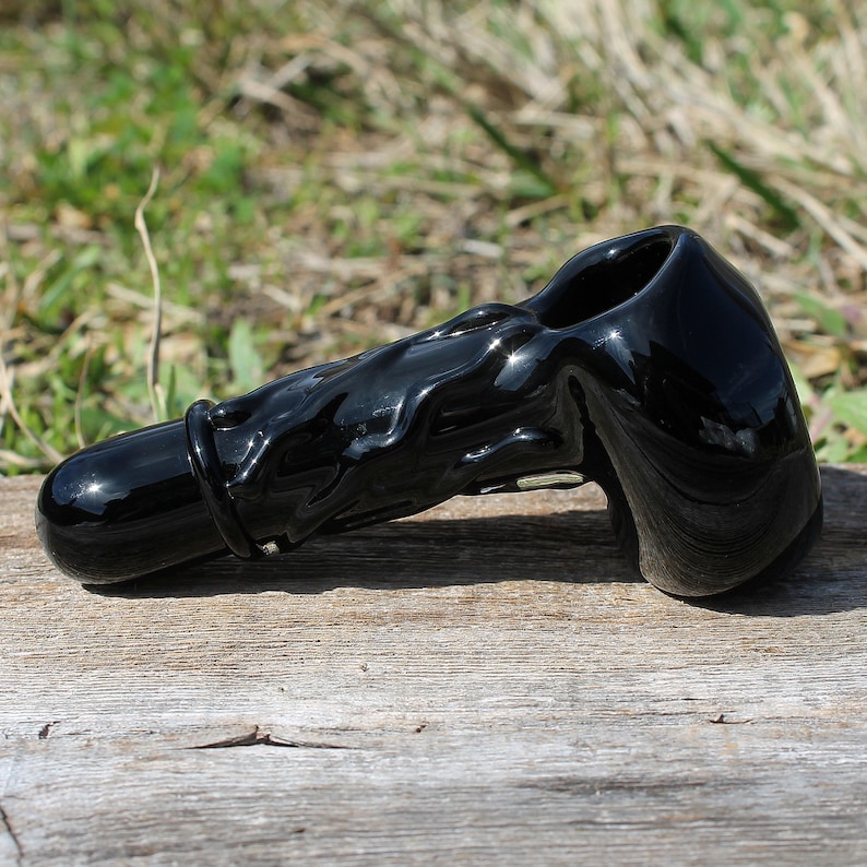 May include: A black glass smoking pipe with a wavy design. The pipe has a bowl on one end and a mouthpiece on the other.