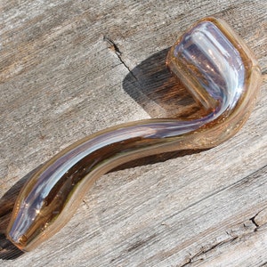 May include: A glass pipe with a curved stem and a rounded bowl. The pipe is made of clear glass with a light brown tint and has a iridescent finish.