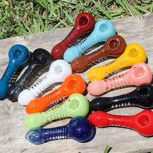 May include: A collection of 14 colorful glass pipes with a spiral design. The pipes are arranged in a row on a wooden surface.