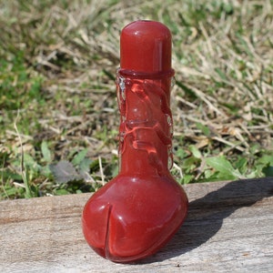 May include: A red glass pipe with a bulbous base and a smooth, rounded top. The pipe has a swirling design.