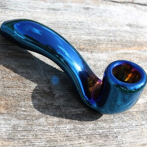 May include: A iridescent blue glass pipe with a curved stem and a round bowl. The pipe has a metallic finish and reflects light.