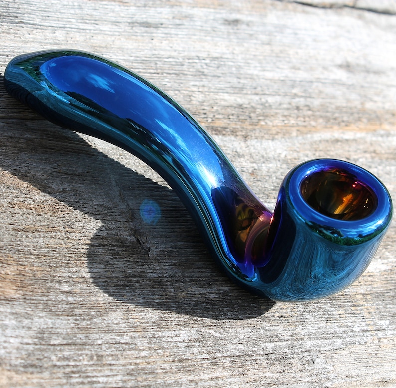 May include: A iridescent blue glass pipe with a curved stem and a round bowl. The pipe has a metallic finish and reflects light.